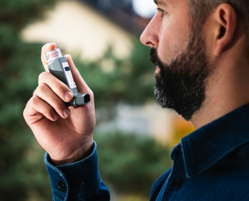 Man managing asthma and allergy symptoms with an inhaler.